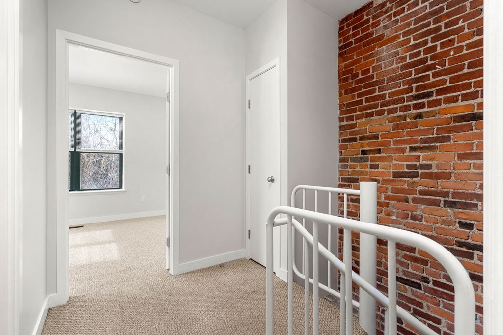 A white door is open to a hallway with a brick wall on the side.