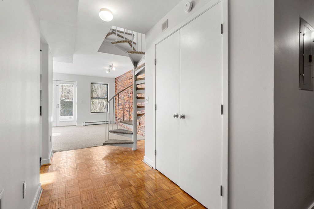 A white hallway with a wooden floor and a staircase.