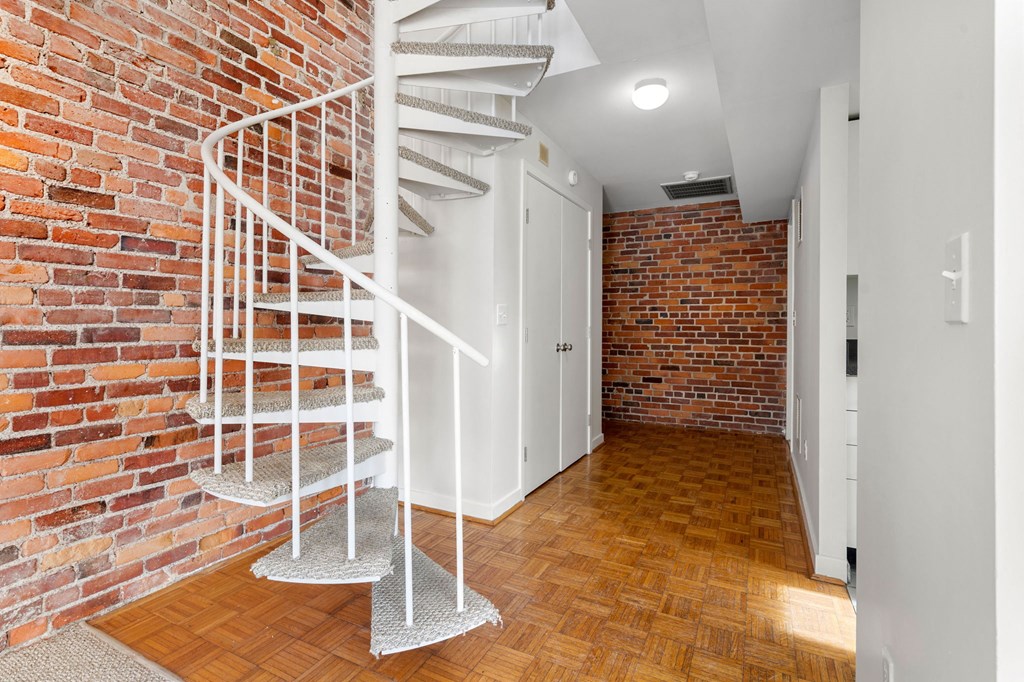 A white spiral staircase with a metal railing is in a room with a brick wall.