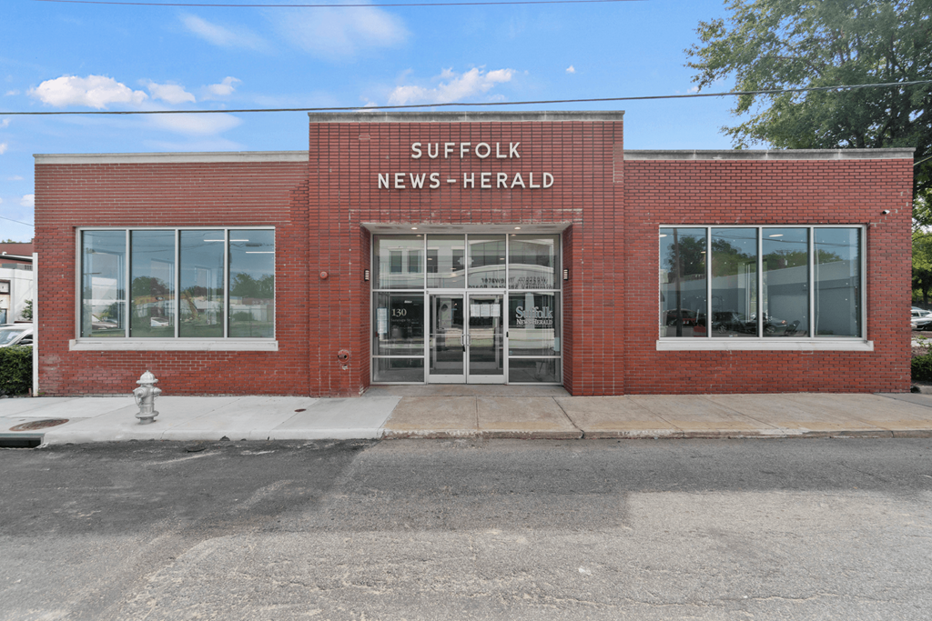 the front of a brick news herald building with a fire hydrant