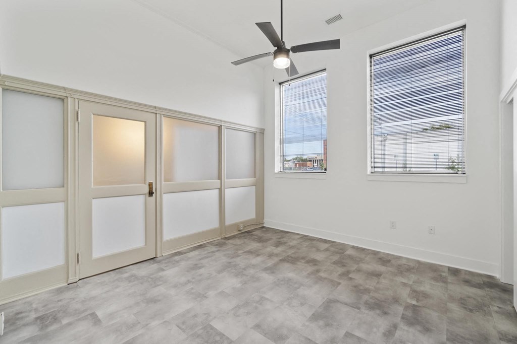 an empty living room with a ceiling fan and two windows