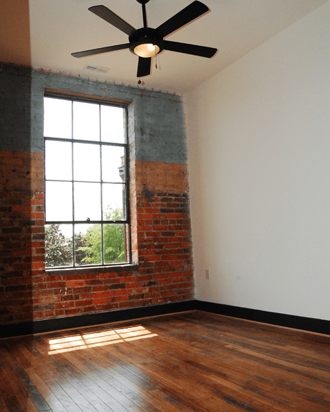A room with a ceiling fan and a window with a brick wall.