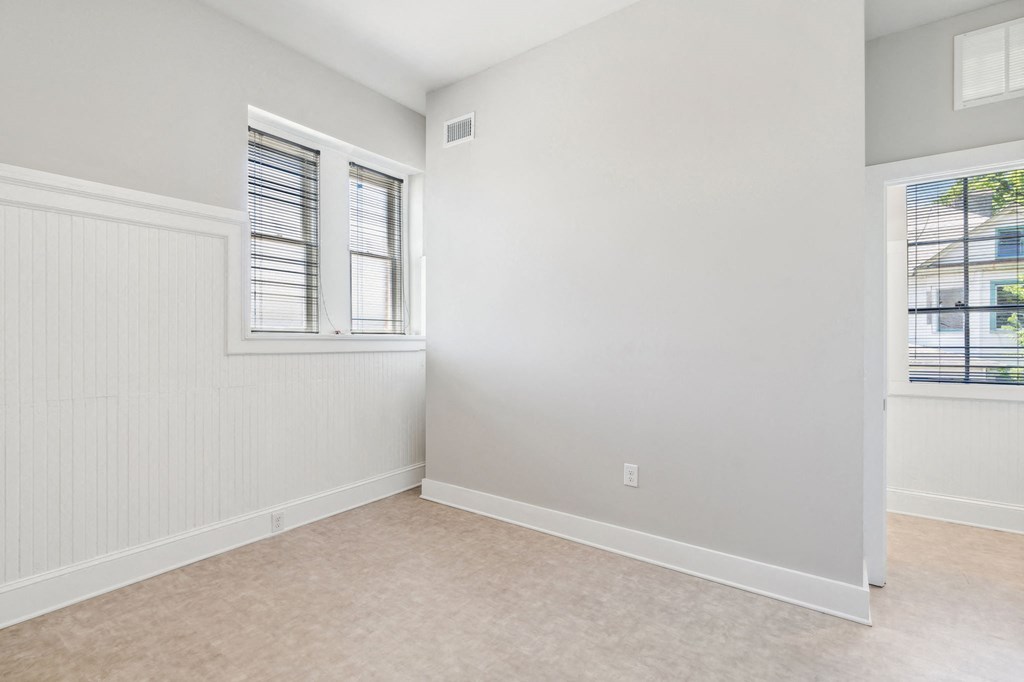 an empty bedroom with two windows and white walls