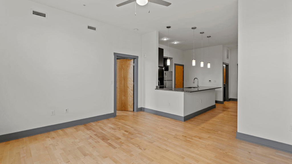 an empty living room and kitchen with wood floors and white walls