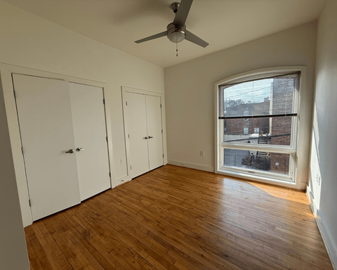 A room with a ceiling fan and a window showing a view of a building outside.
