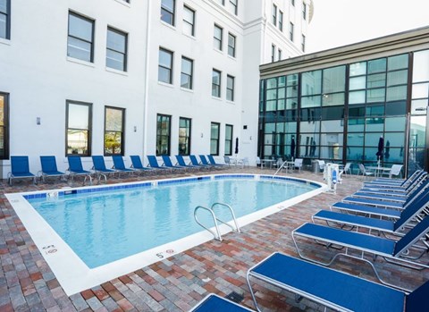 A pool surrounded by blue chairs and a white building in the background.