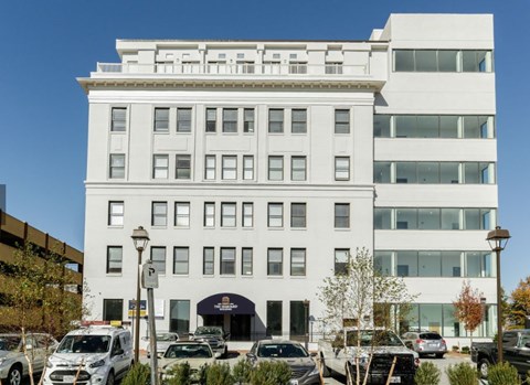 A white building with a black awning and cars parked in front.
