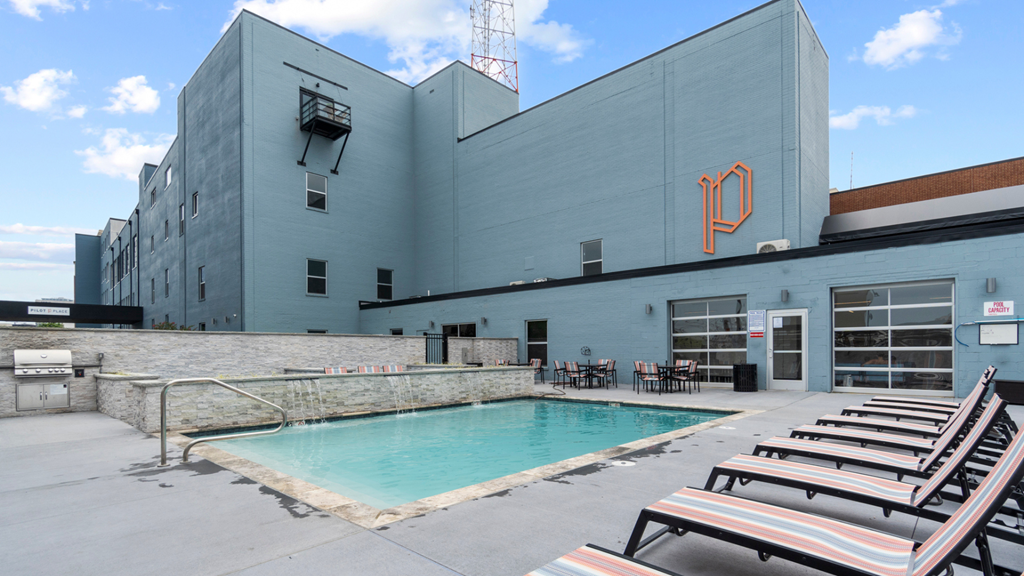 a swimming pool in front of a blue building with beach chairs
