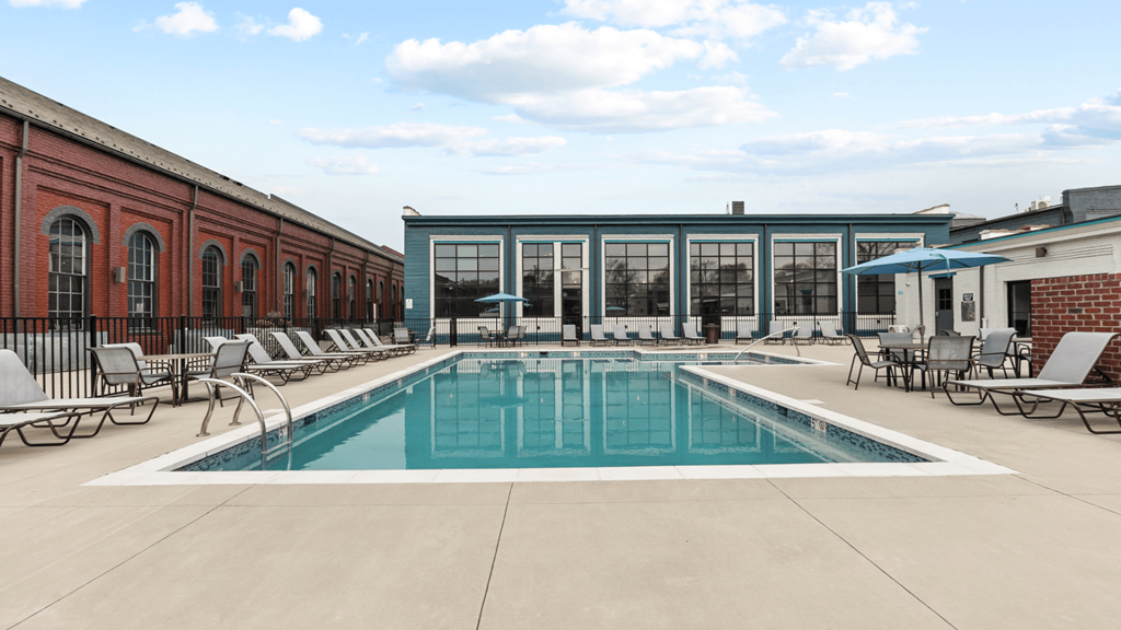 a swimming pool with lounge chairs and umbrellas in front of a brick building