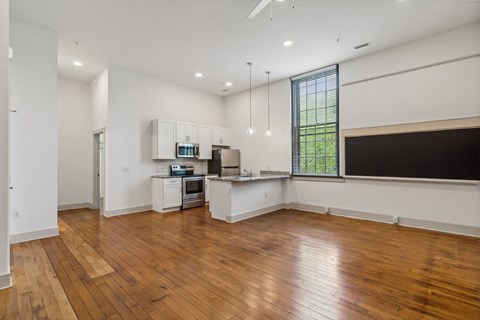 an empty living room with a kitchen and a large window