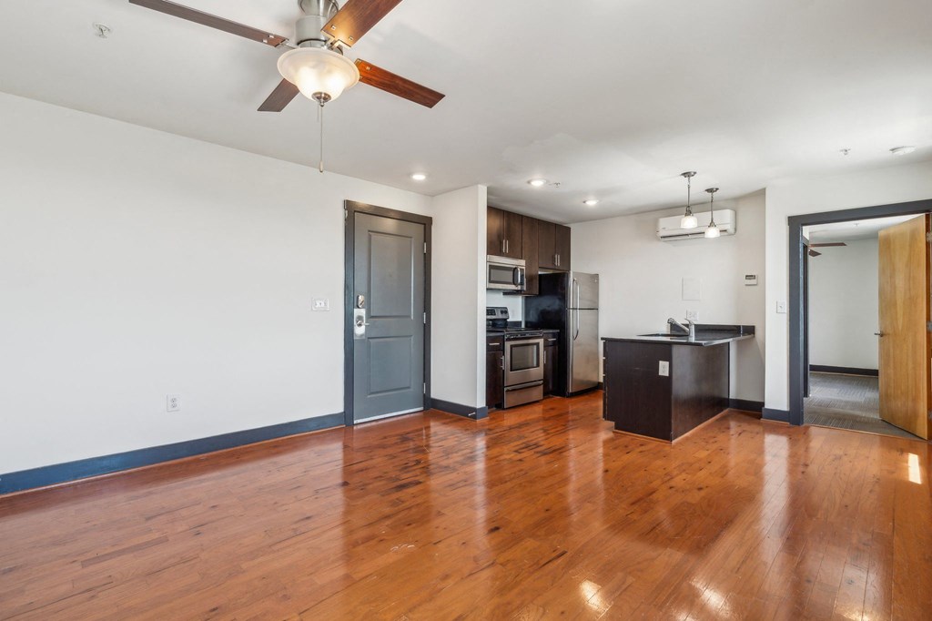 an empty living room and kitchen with wood floors and a ceiling fan