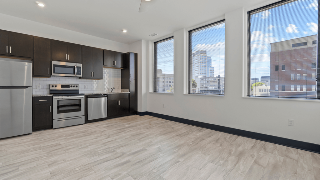 the living room of an apartment with a kitchen and large windows