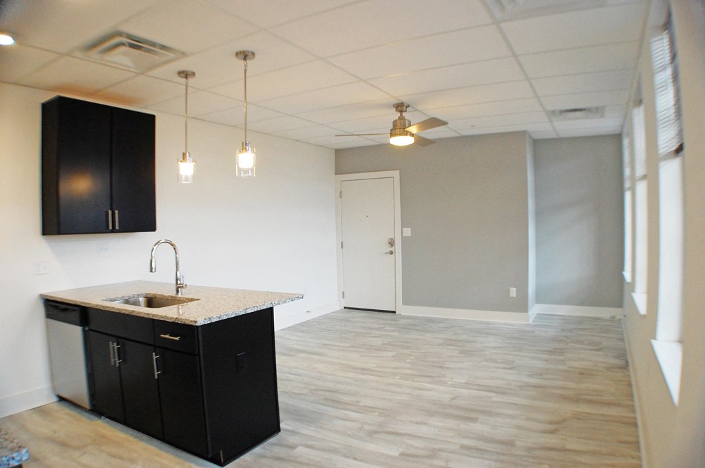 an empty living room with a kitchen and a ceiling fan