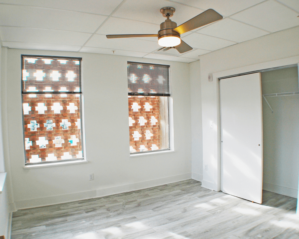 A room with a ceiling fan and two windows.