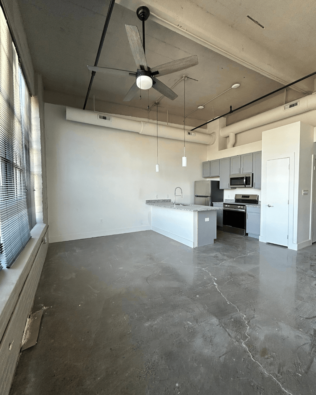an empty living room with a ceiling fan and a kitchen