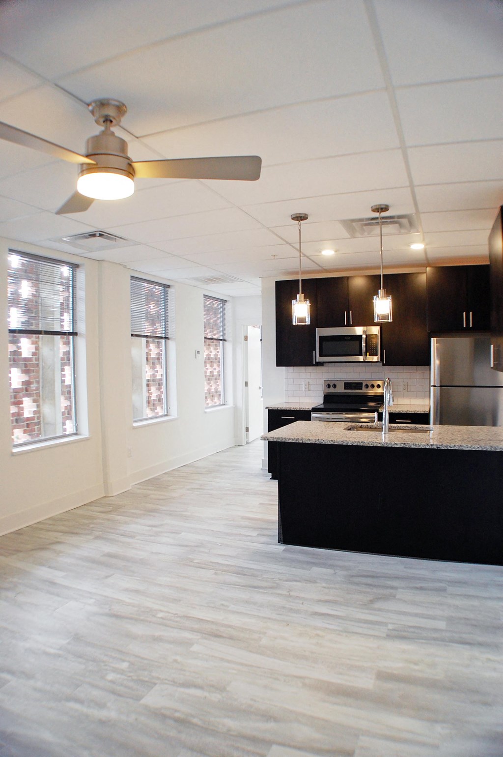 an empty living room with a kitchen and a ceiling fan