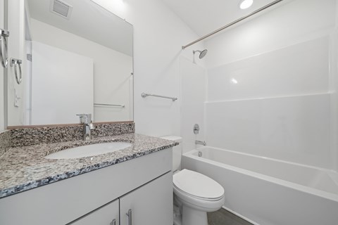 A white bathroom with a granite countertop and a white toilet.
