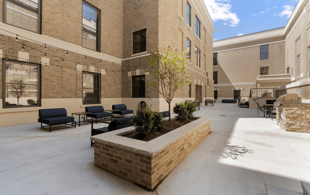 a courtyard with tables and chairs and a tree in front of a building