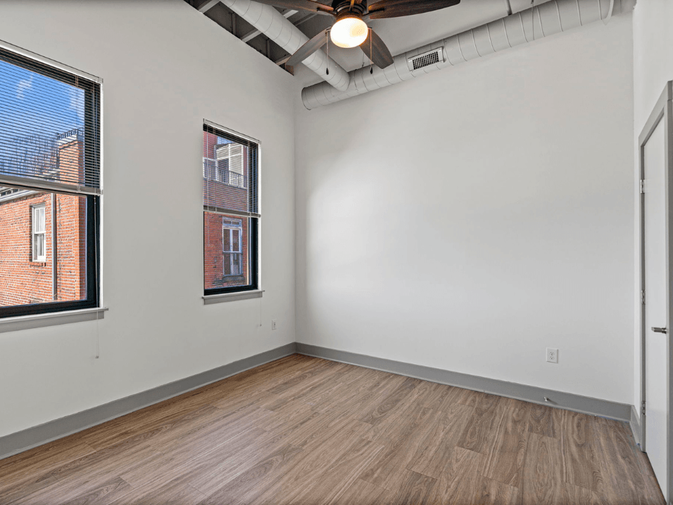 the living room of an empty apartment with wood flooring and two windows