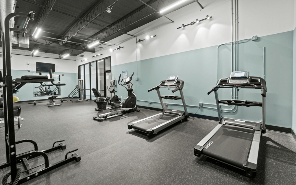a gym with cardio equipment and weights on the floor and a green wall