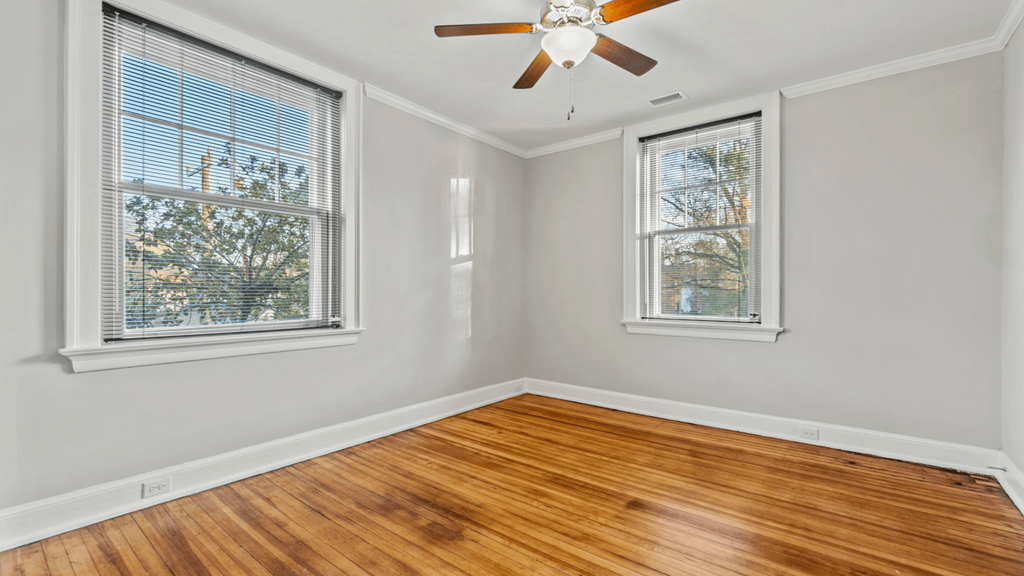 an empty bedroom with two windows and a ceiling fan