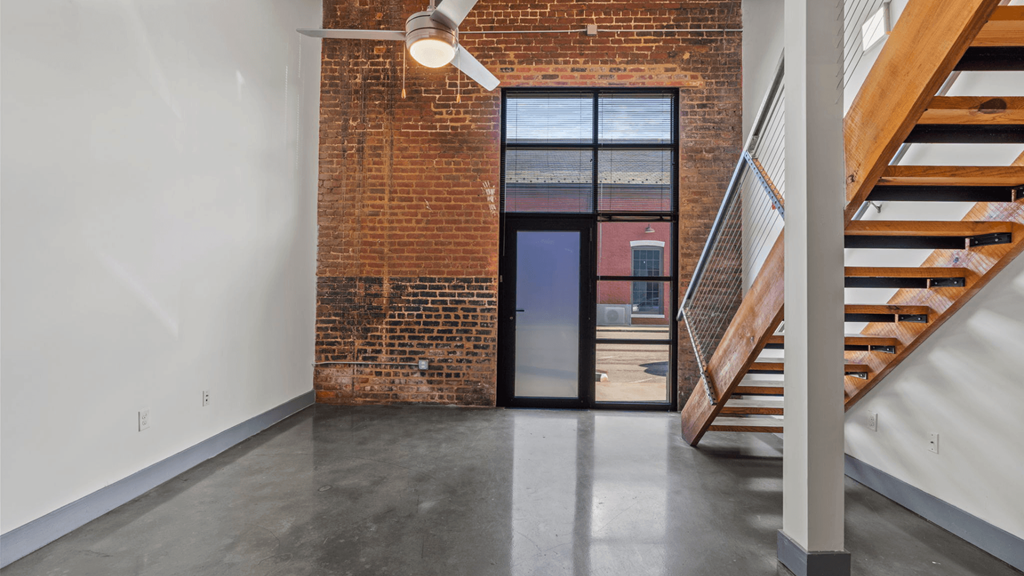 a living room with a staircase and a brick wall and a glass door