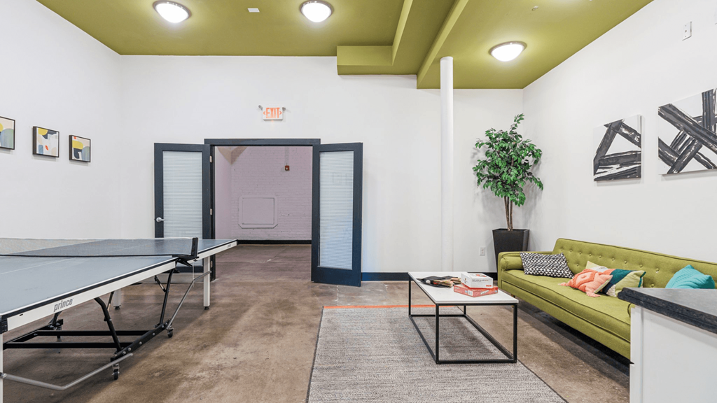 A room with a ping pong table and a green couch.