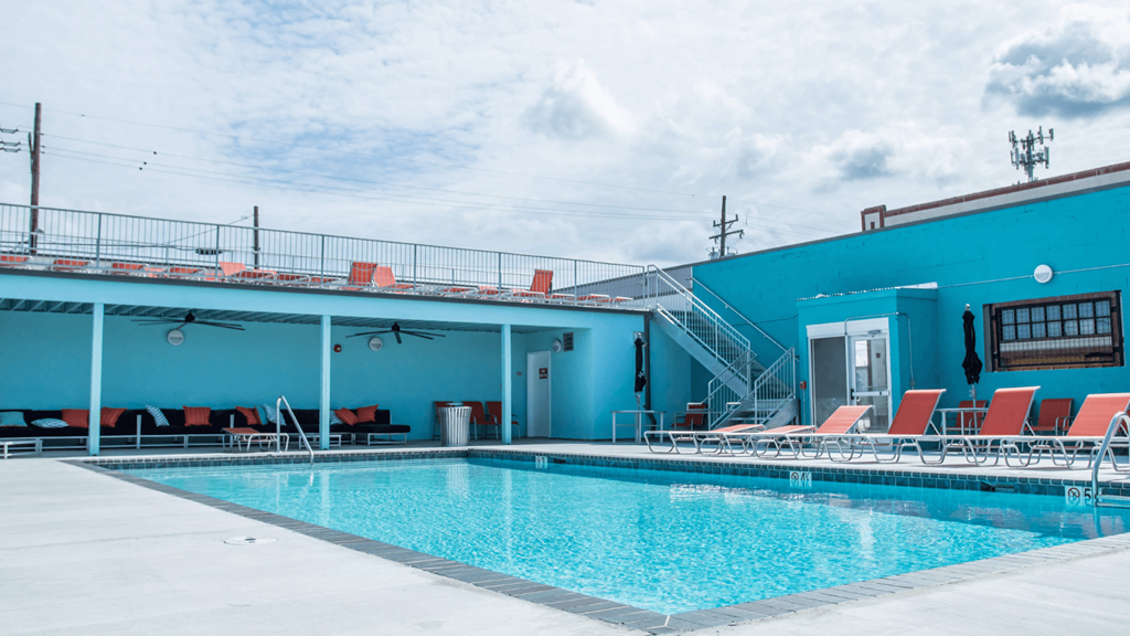 A swimming pool with red lounge chairs and a blue building in the background.