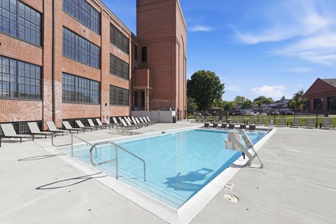 A swimming pool on a rooftop with lounge chairs and a building in the background.