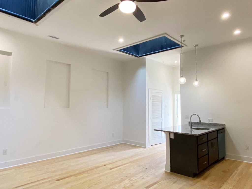 an empty living room with a kitchen and a ceiling fan