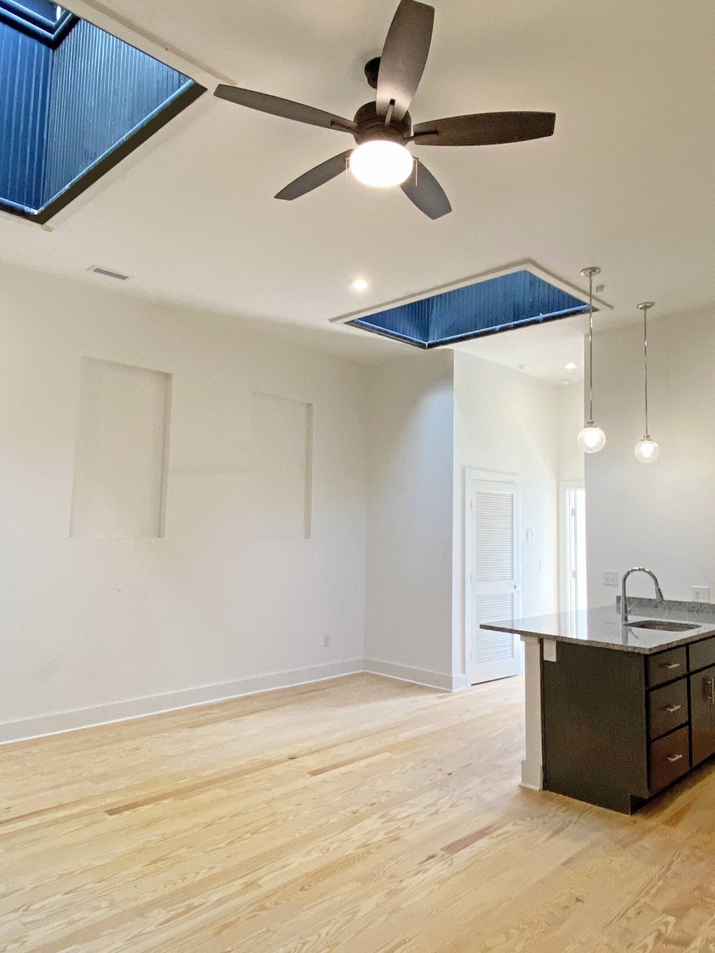 an empty living room with a ceiling fan and a kitchen