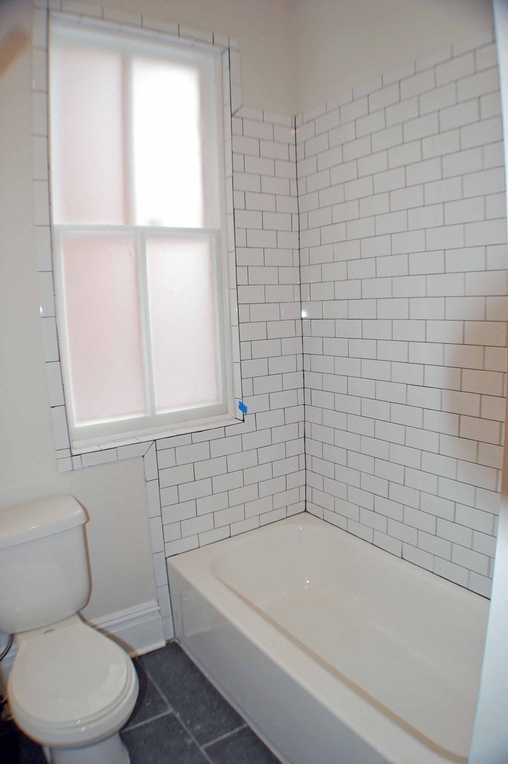 A white toilet sits next to a bathtub in a bathroom with white tiles.
