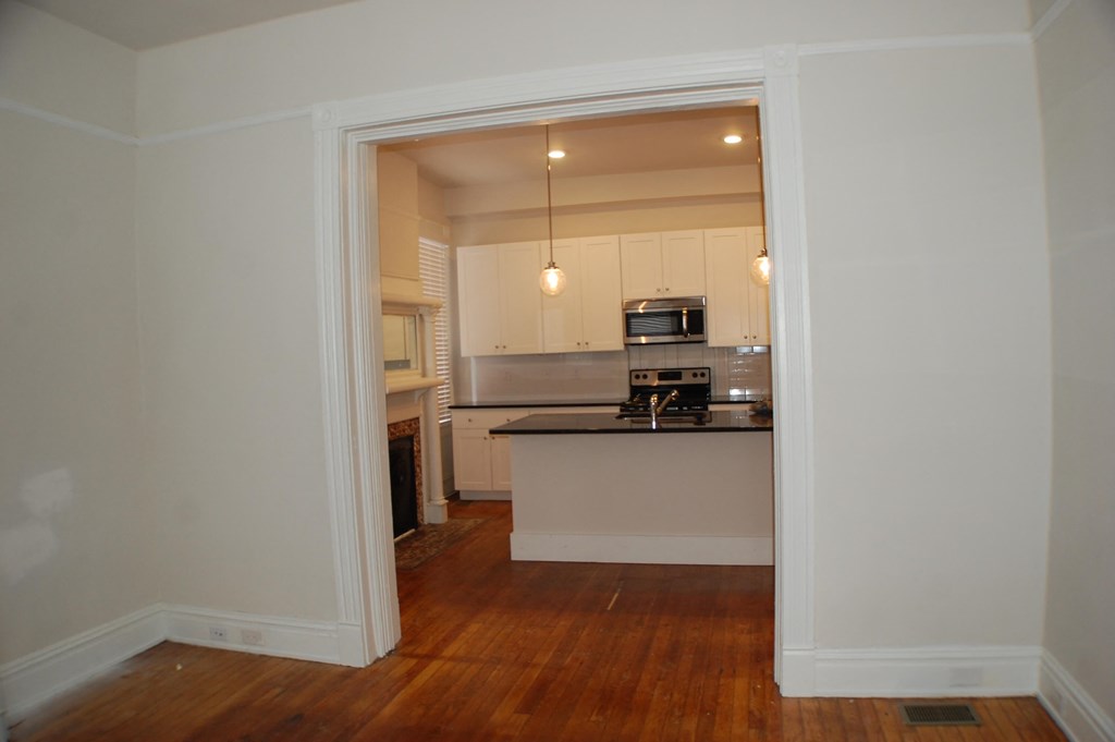 A kitchen with white cabinets and a black countertop is visible through an open doorway.