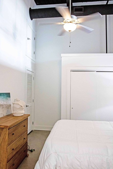 A bedroom with a bed, dresser, and ceiling fan.