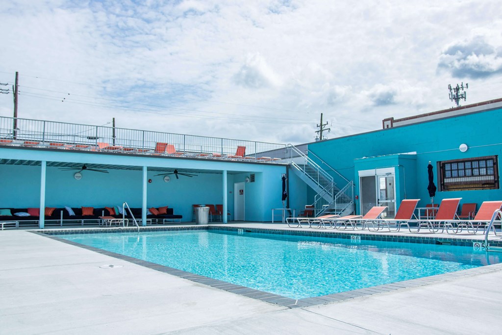 A large swimming pool with red lounge chairs and a blue building in the background.