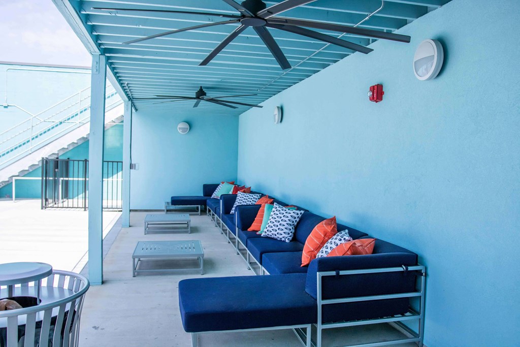 A blue couch with pillows and a fan on the ceiling.