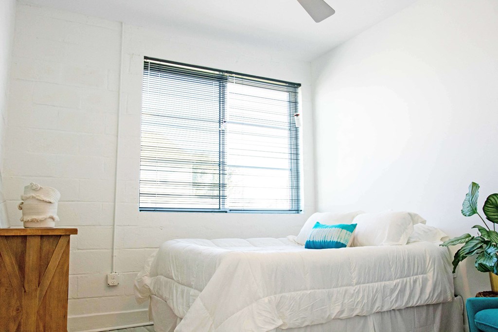 A white bedroom with a bed, pillows, a nightstand, and a plant.