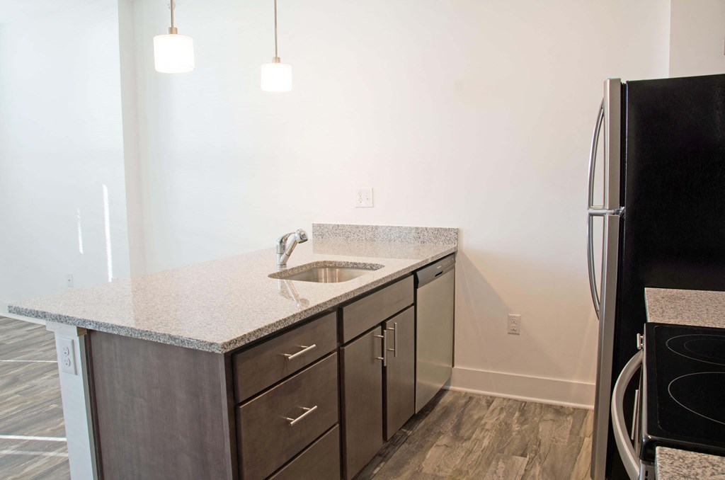 A kitchen with a black refrigerator and a sink with a granite countertop.