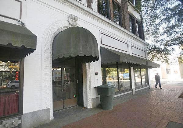 A white building with a black awning and a man walking in front.