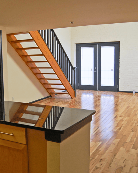 A wooden staircase with a black railing leads to a white door.