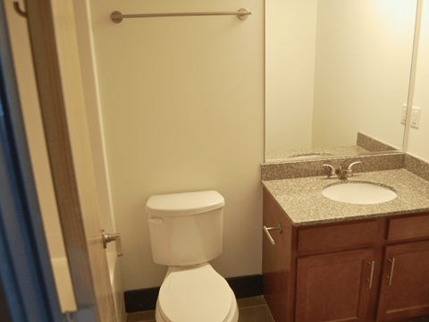 A white toilet is in a bathroom with a granite counter top.