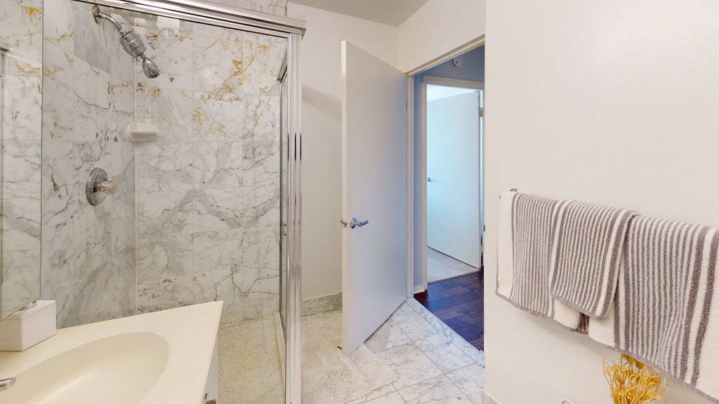A bathroom with a marble shower, white sink, and a towel rack at 10 West Apartments, Long Beach, NY, 11561