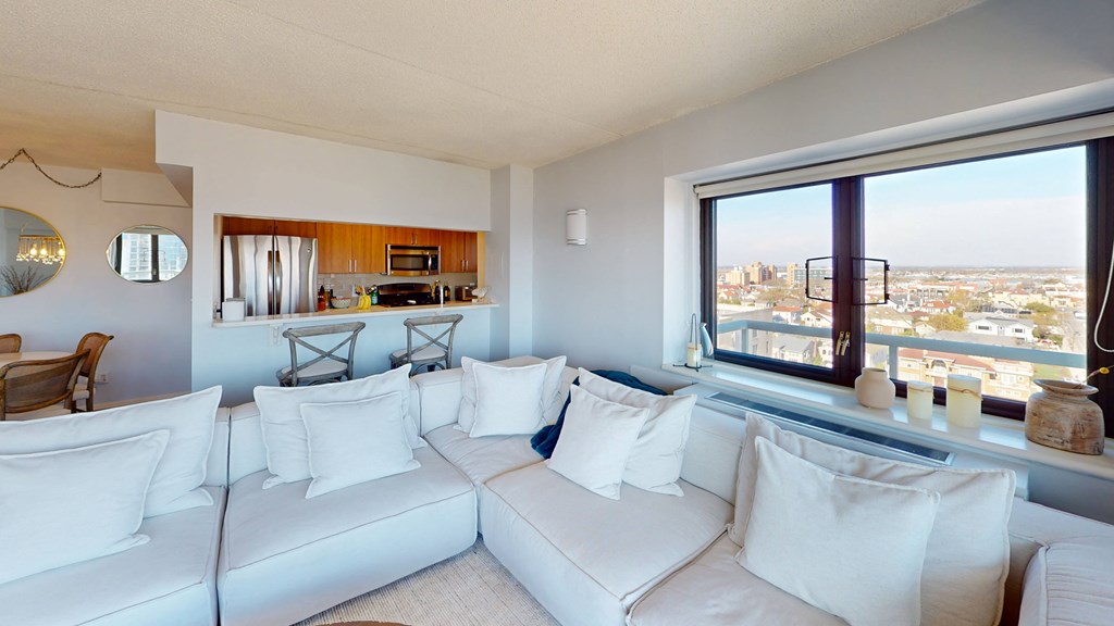 A white couch with pillows sits in a living room with a view of the city at 10 West Apartments, New York 11561