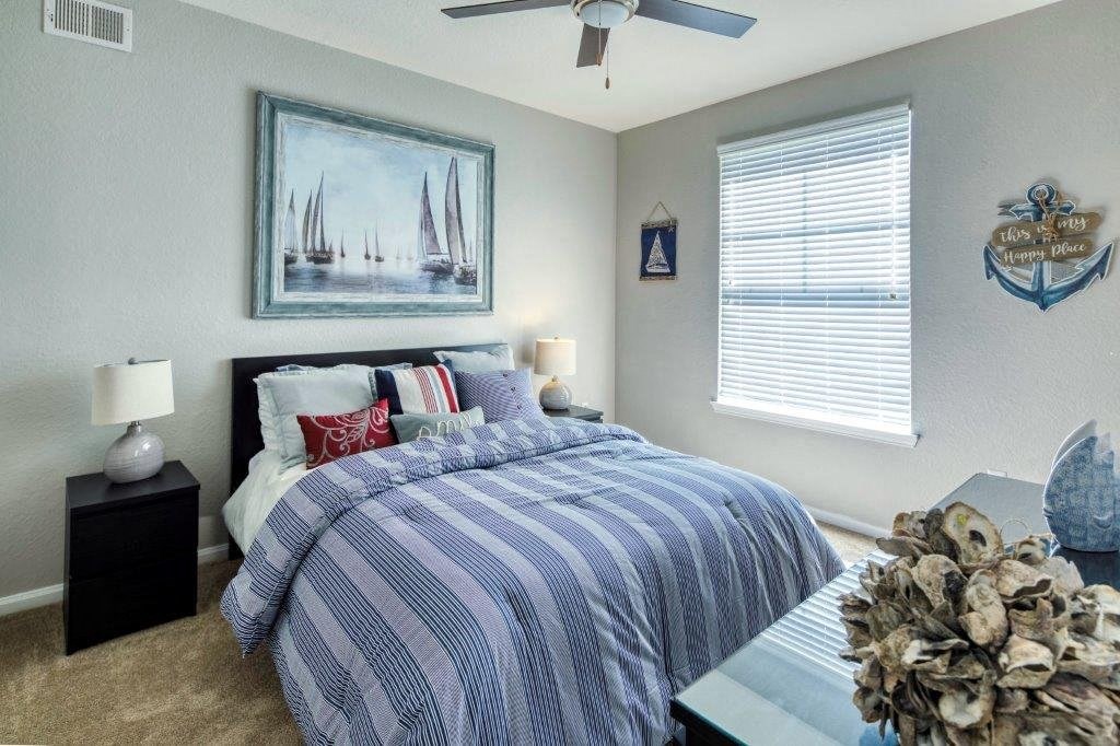 A bedroom with a bed, a ceiling fan, and a painting of sailboats on the wall. A bedroom with a bed, a ceiling fan, and a painting of sailboats on the wall at Rivertree Apartments, Riverview, Florida