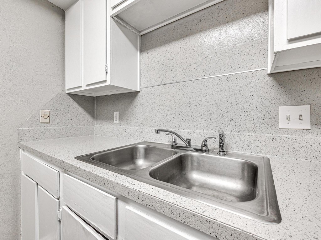 a stainless steel sink in a kitchen with white cabinets