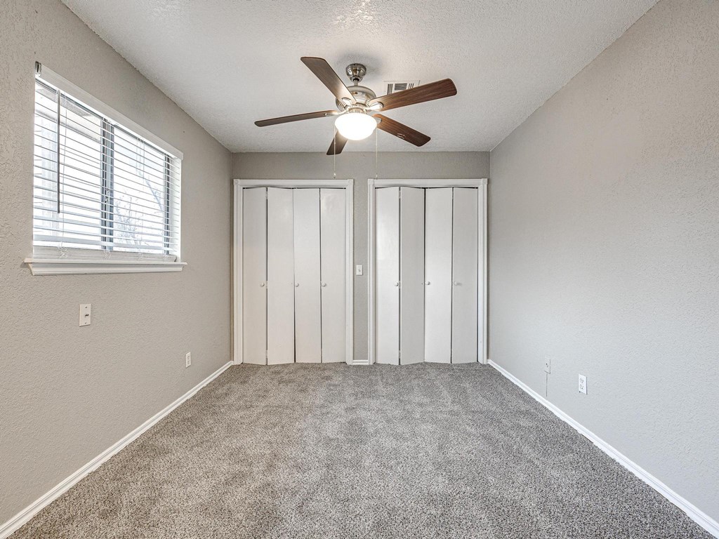 an empty bedroom with a ceiling fan and a window