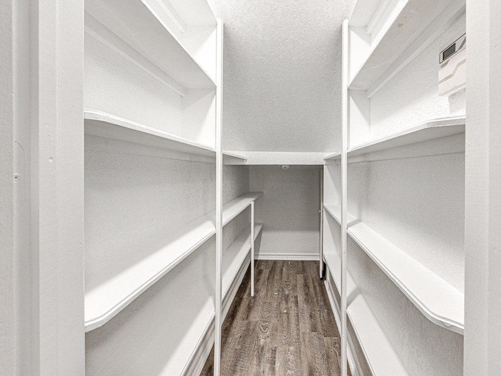 a walk in closet with white shelves and a wood floor