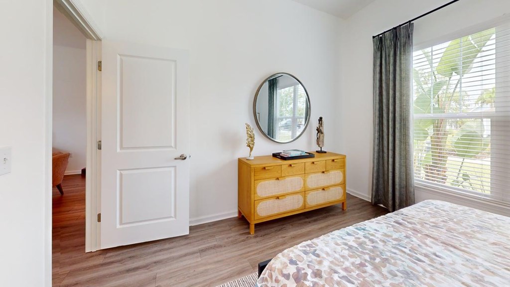 A bedroom with a bed, a dresser with a mirror, and a window with curtains.