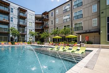 a swimming pool with yellow and green chairs in front of an apartment building at Artisan Twickenham Square, Huntsville, AL 35801