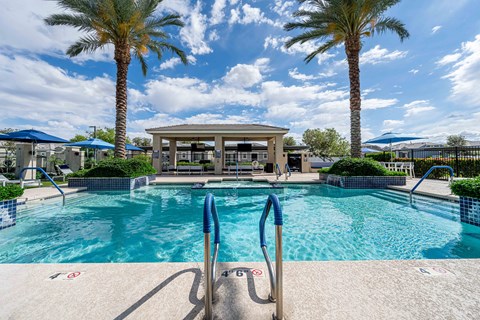 A pool surrounded by palm trees and a pavilion. at Vistoria At Country Place Apartments, Tolleson